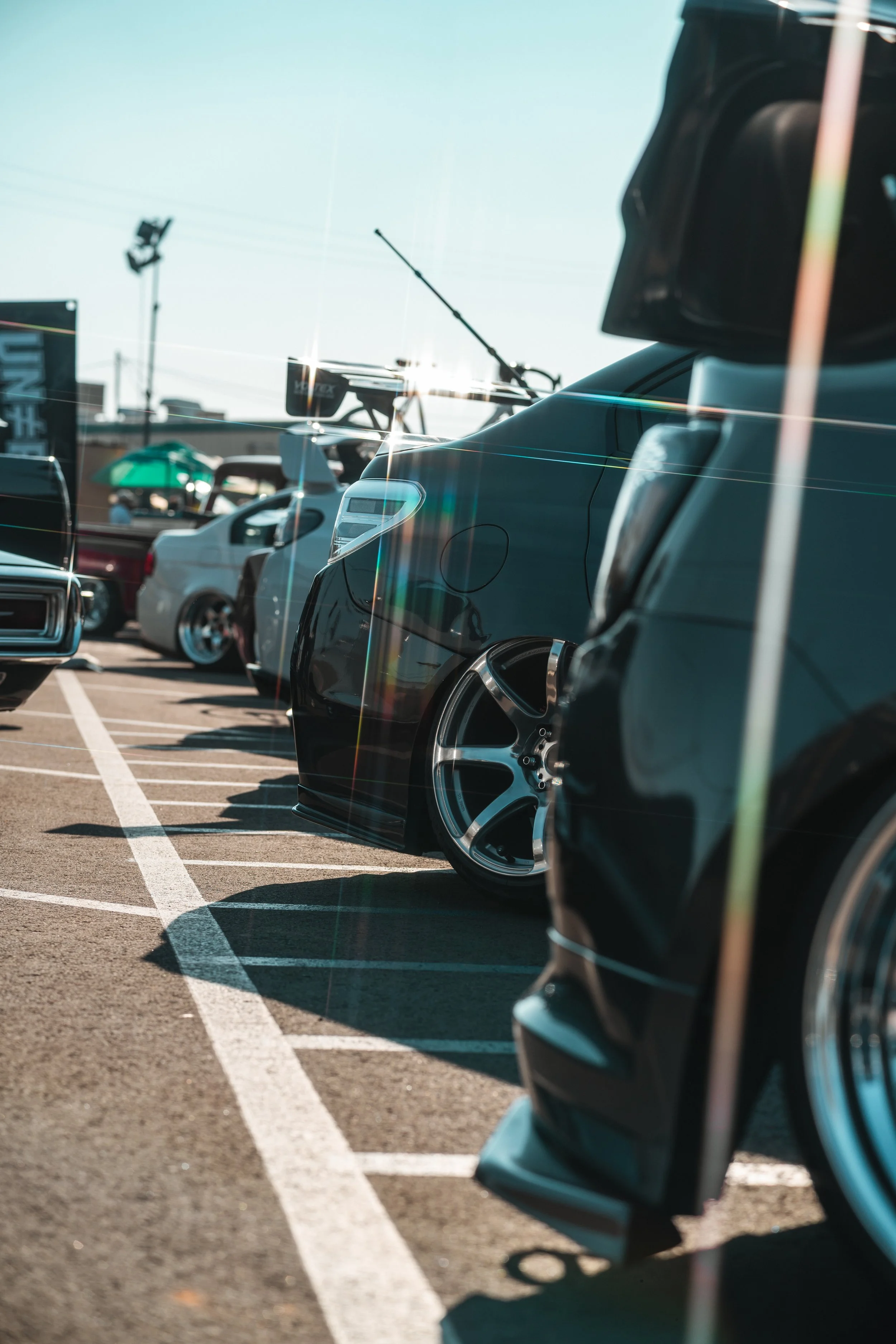 A row of parked cars in a parking lot with sunlight reflecting off the vehicles and lens flare visible.
