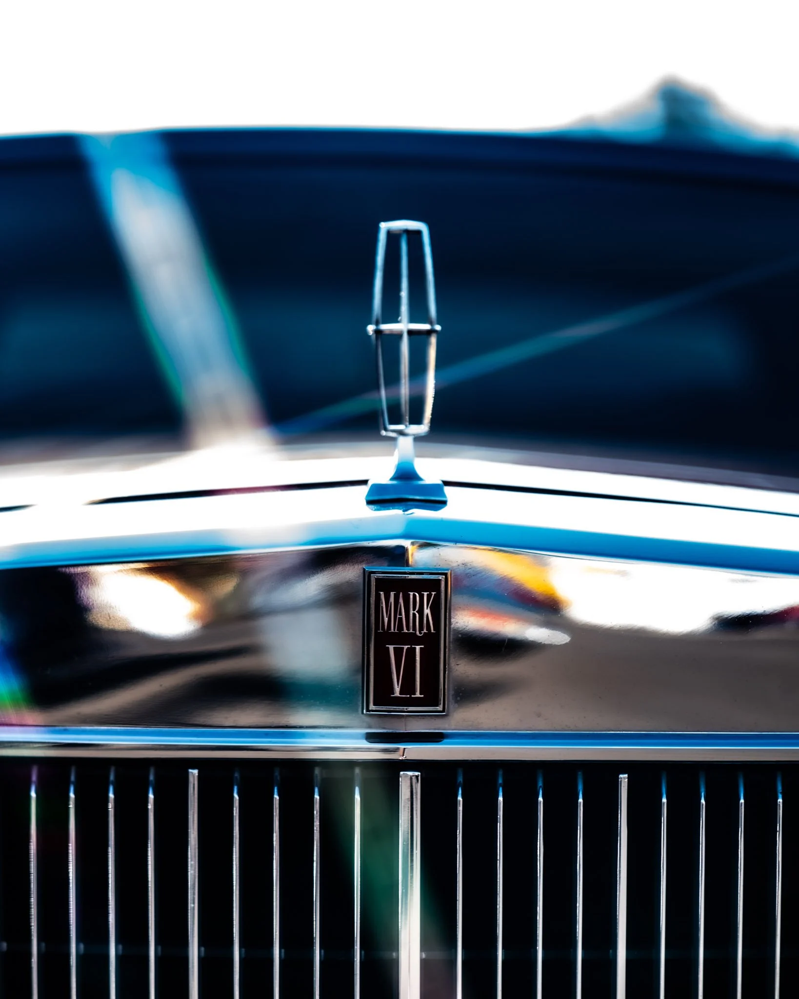 Close-up of a stainless steel car badge with the Renault logo, mounted on the front grille of a vehicle. The badge reflects light and the word 'MARK VI' is visible below it.