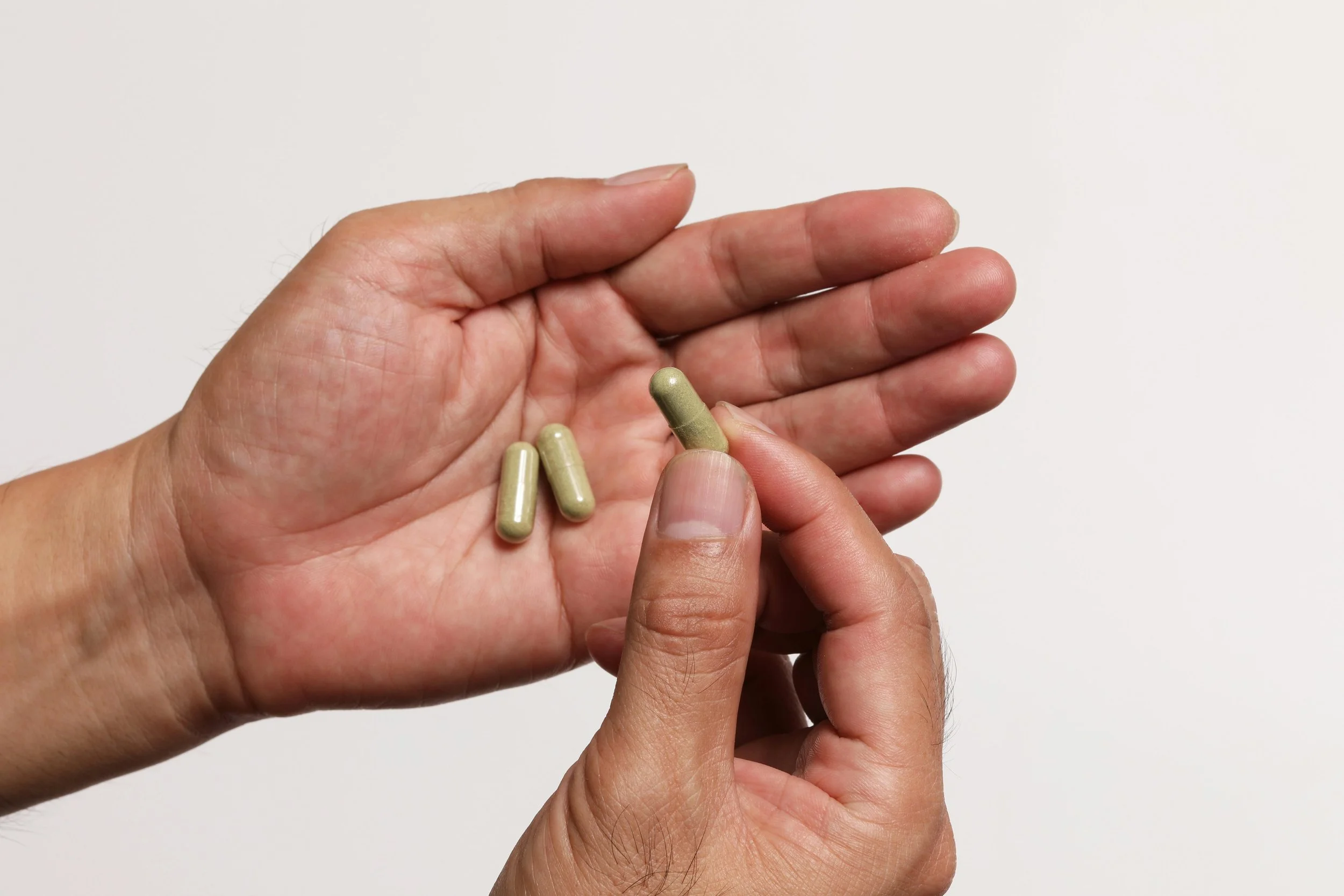 Close-up of a person holding three beige capsules in their hand against a plain white background.