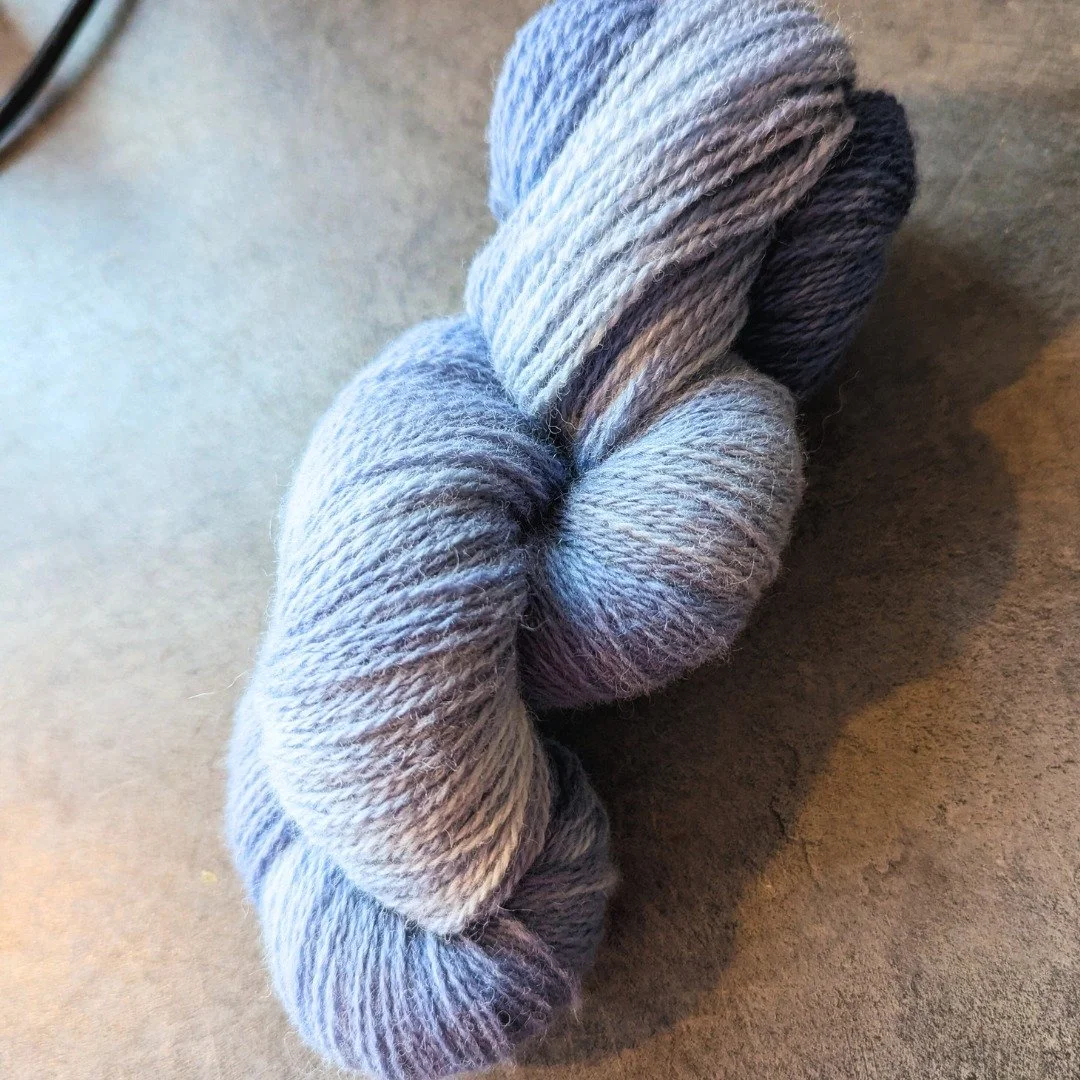 A skein of twisted gray and black yarn on a flat surface.