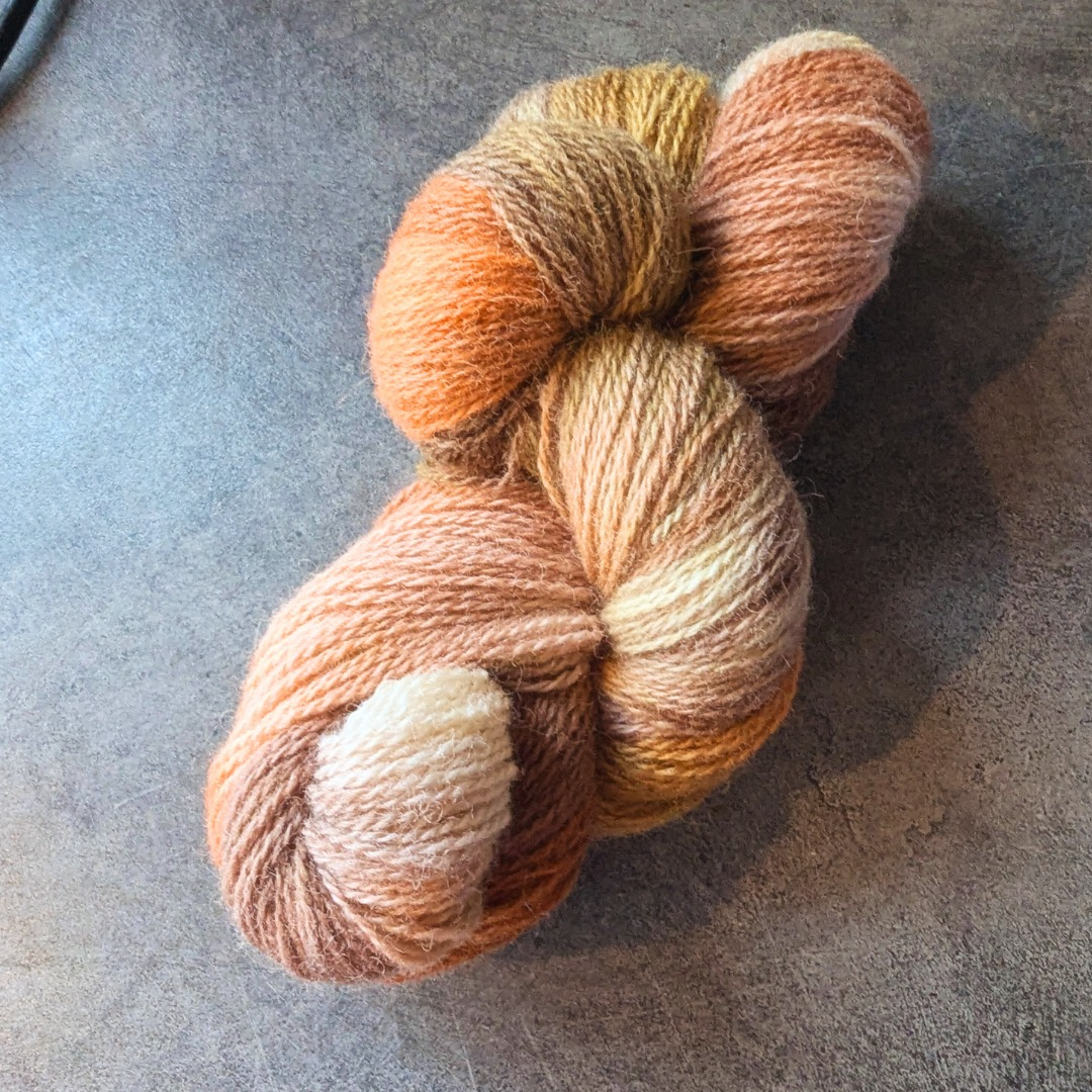 Multicolored skein of yarn in shades of orange, brown, beige, and pink.
