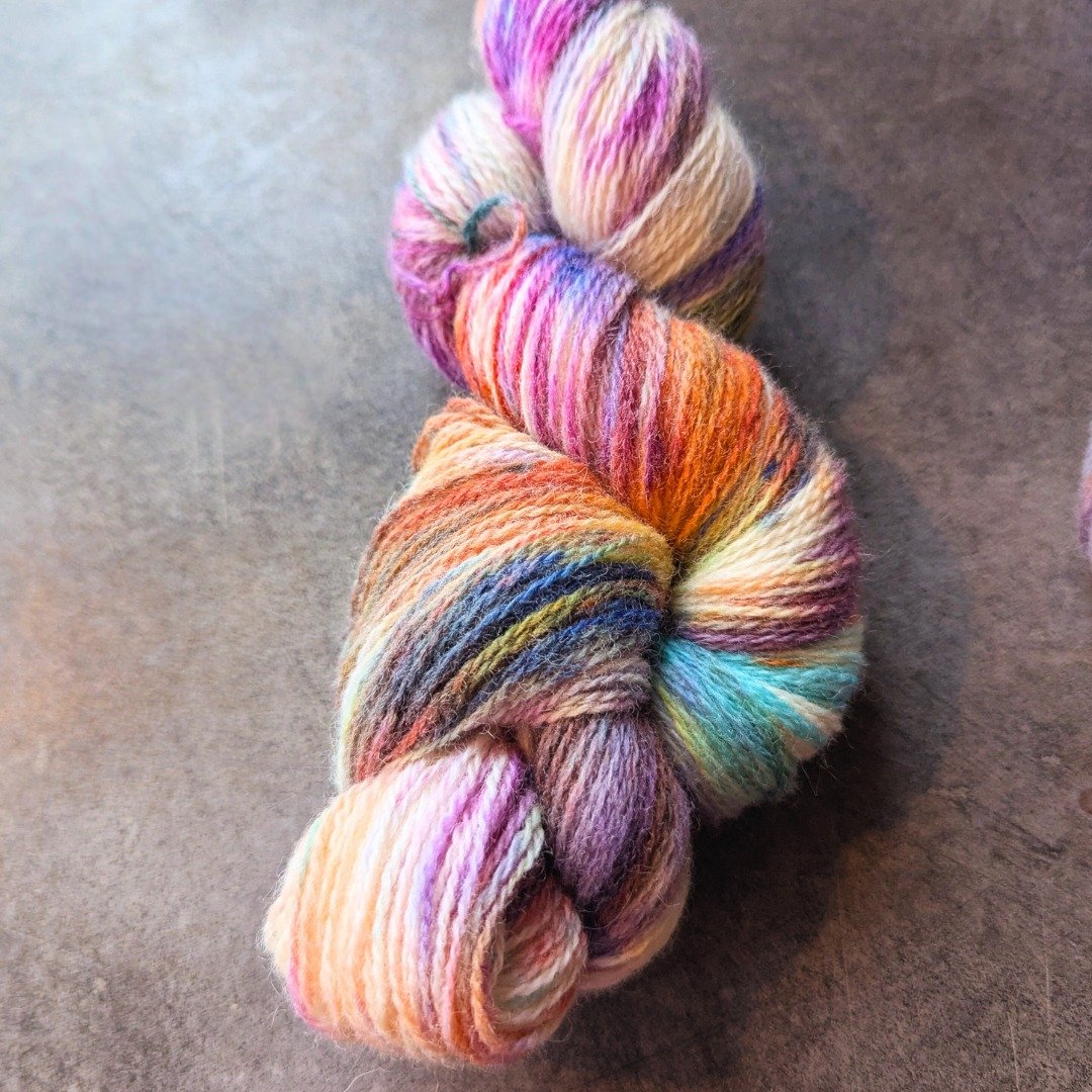 Colorful skein of hand-dyed yarn with various shades including pink, purple, orange, blue, and cream, twisted into a hank.