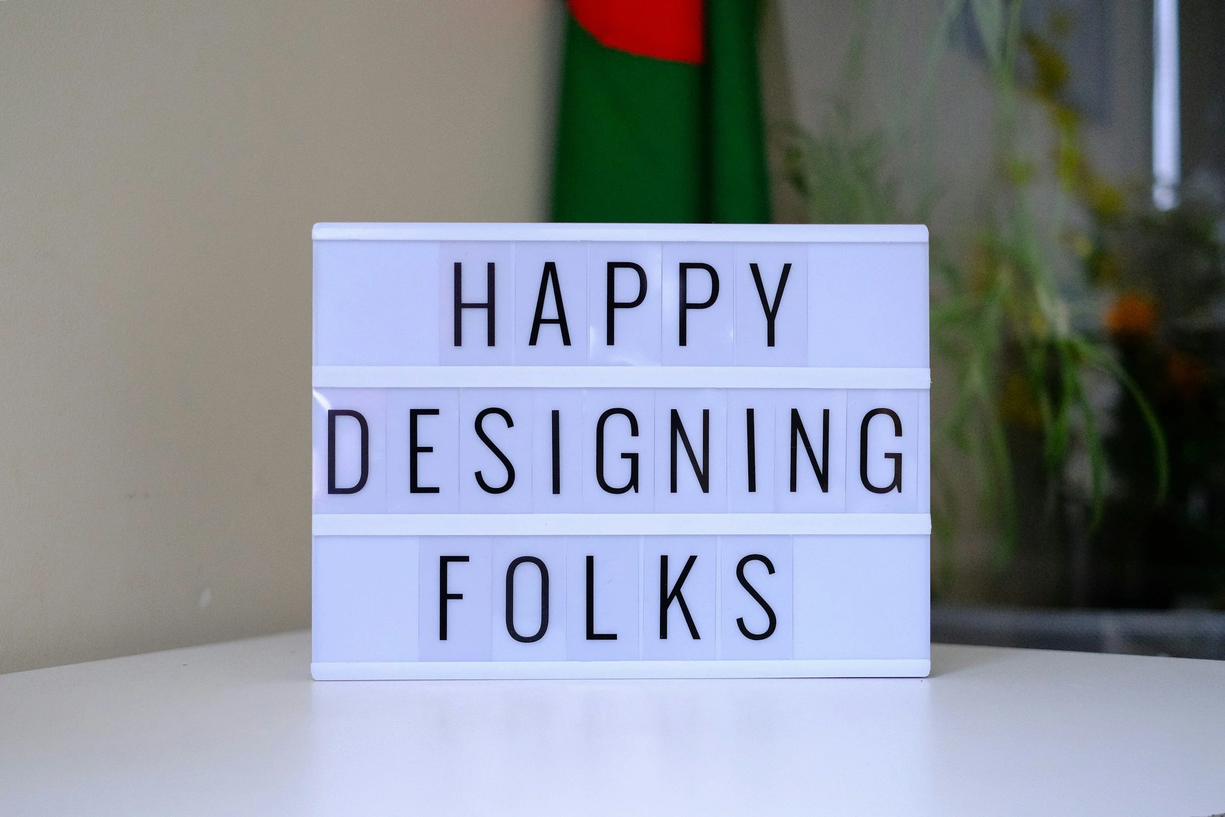 A lightbox sign on a white table spells out "HAPPY DESIGNING FOLKS" with black letters on a white background.