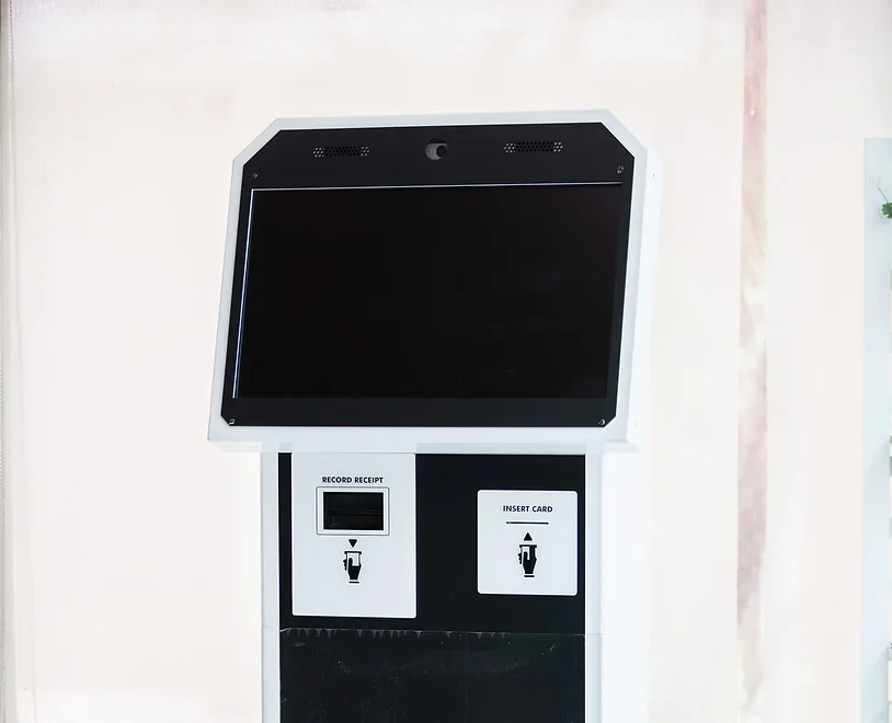 A black and white kiosk with a large blank screen, a card insertion slot, and a receipt recording slot