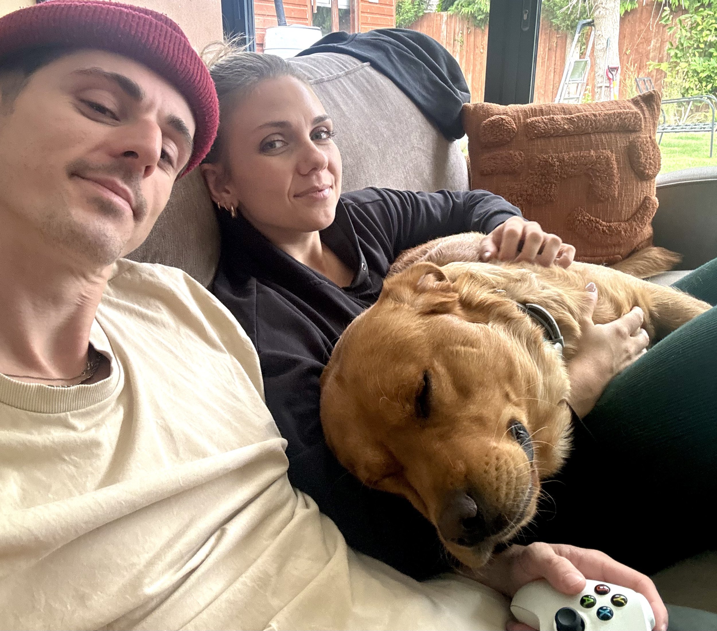 A man and woman sitting on a couch with a Golden Retriever dog, which is sleeping on the woman's lap.