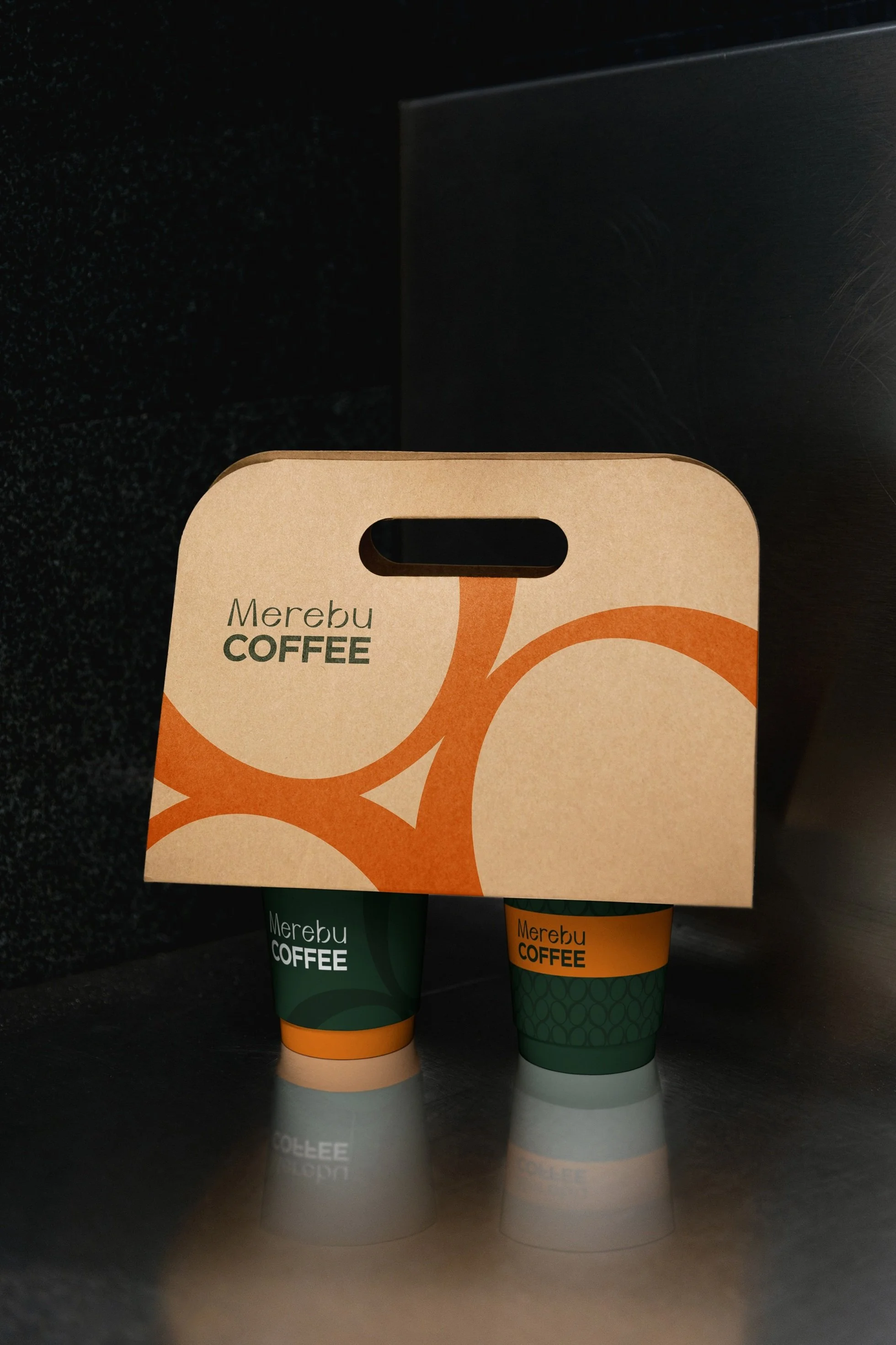 Design papírových kelímků a kartonového nosiče (takeaway) pro kavárnu Merebu. Aplikace brandingu a loga na spotřební obaly.