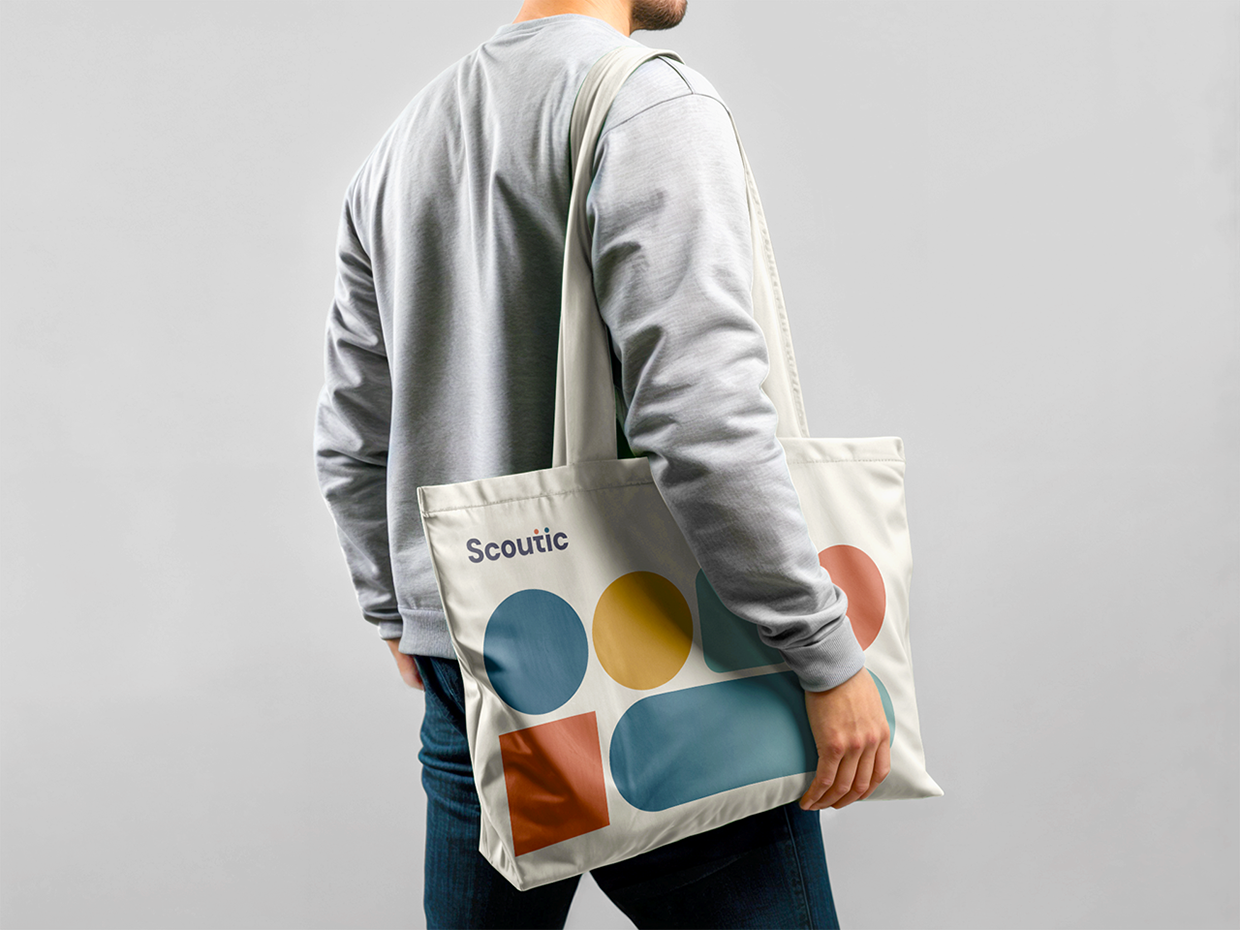 Muž nesoucí plátěnou tašku (tote bag) s abstraktním grafickým motivem značky Scoutic. Ukázka aplikace brandingu na textil a reklamní předměty.