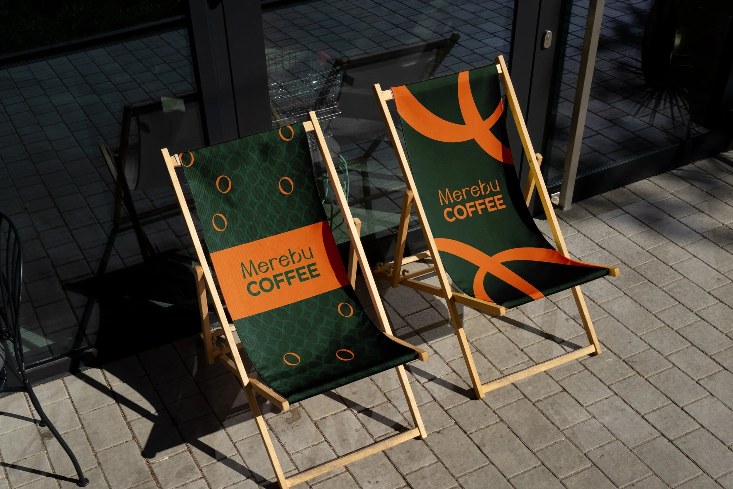Branding reklamních lehátek před kavárnou. Ukázka aplikace firemních barev (zelená a oranžová) na exteriérový nábytek.