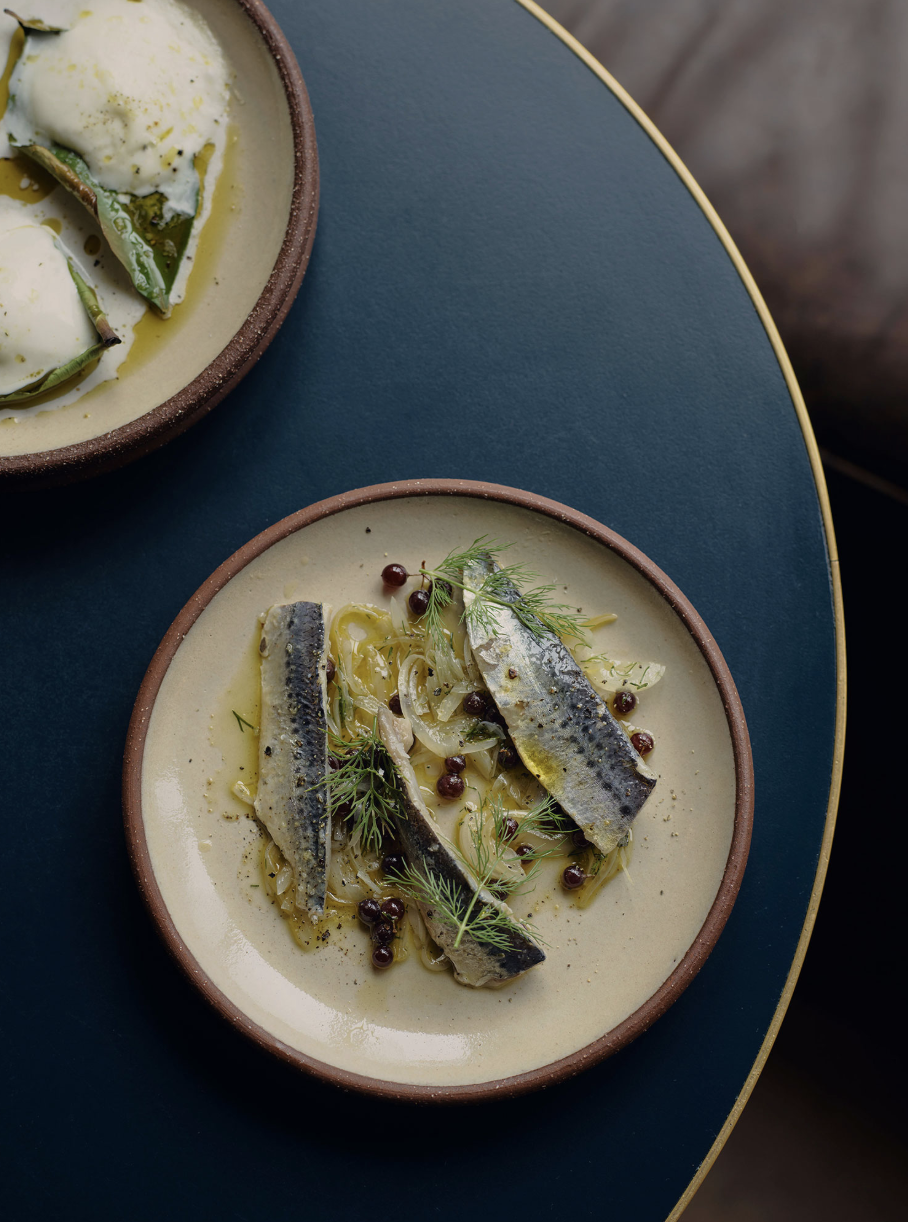 Bowls of fish in creamy sauce, garnished with herbs and berries, on a dark blue plate.