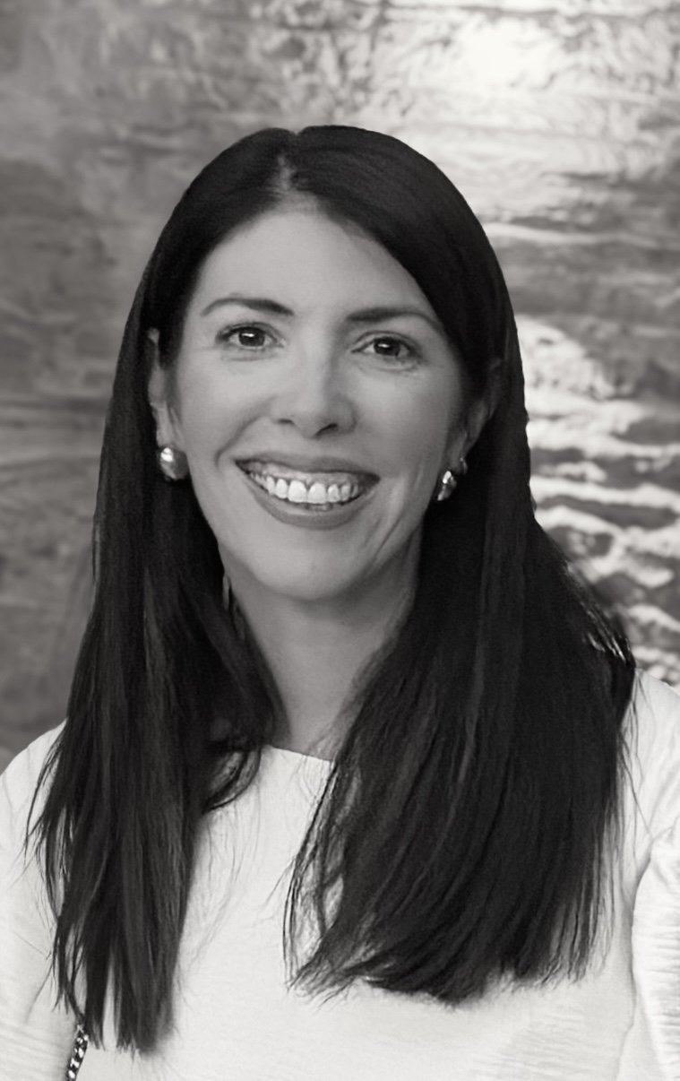 Black and white portrait of a woman with long dark hair, smiling, wearing earrings, in front of a textured background.