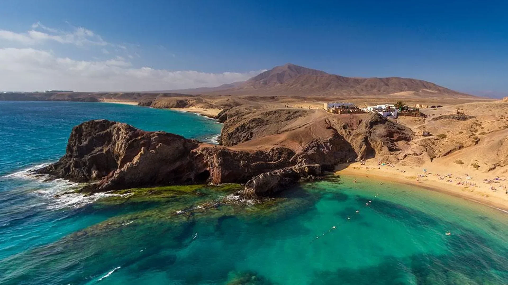 A wide volcanic coastline in soft, low winter sunlight, gold light on dark sand, no people.
