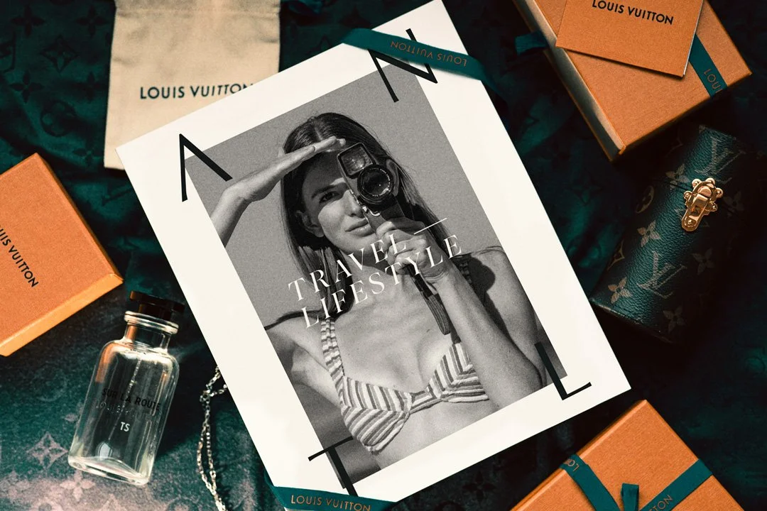 A black and white magazine cover titled "Travel & Lifestyle" surrounded by Louis Vuitton boxes, a perfume bottle, and accessories.