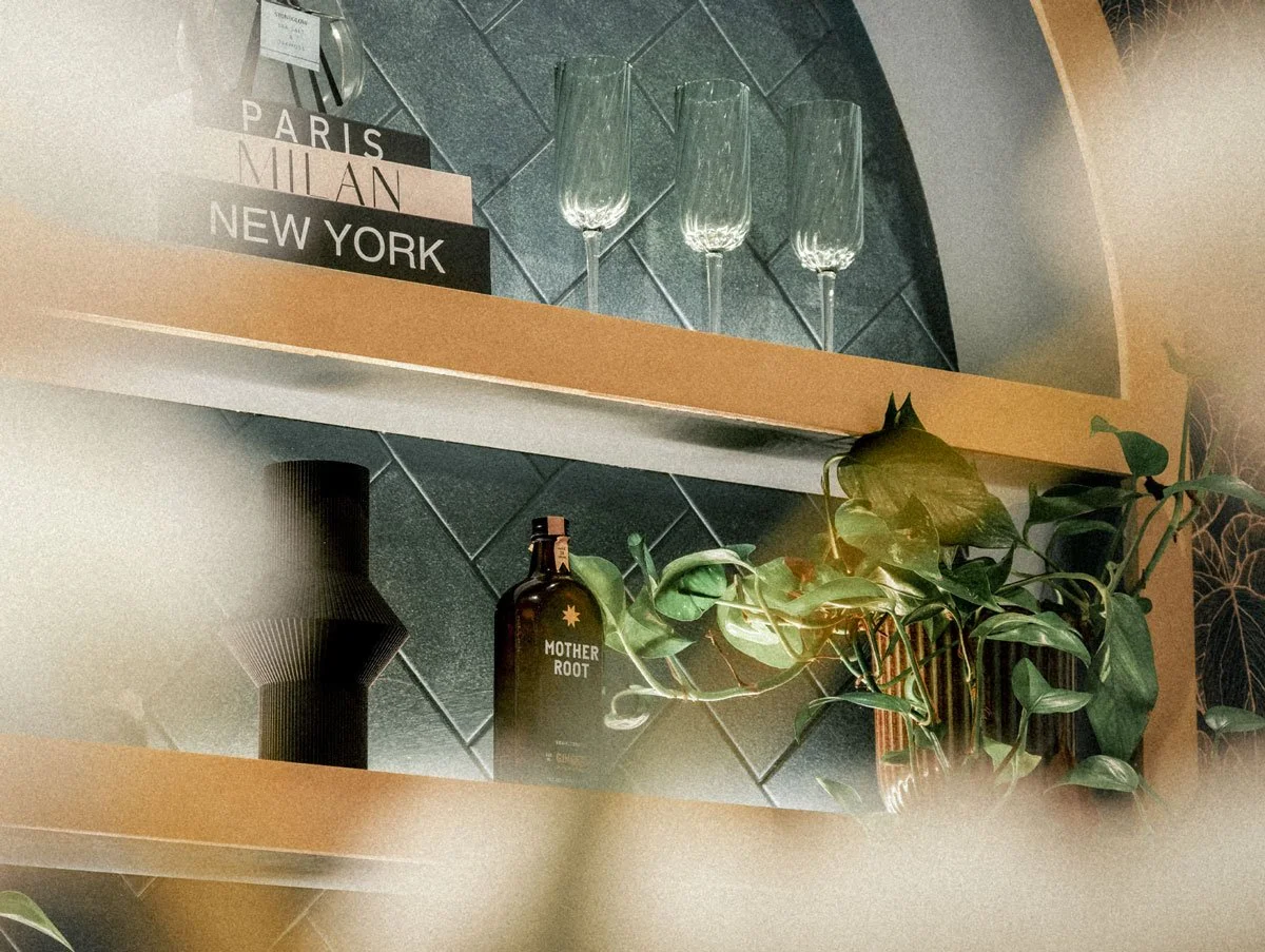 Shelves with decorative glassware, a plant, candles, and a box labeled 'Mother Root' in a modern kitchen setting.