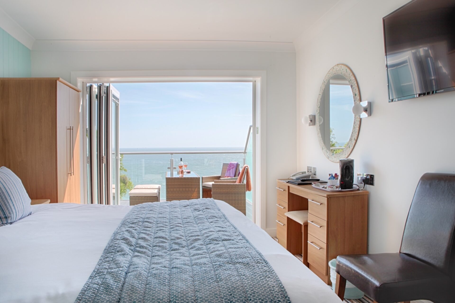 A Superior Sea-Facing Room at Luccombe Hall with a double bed, a dressing table and open doors to a balcony over the sea.