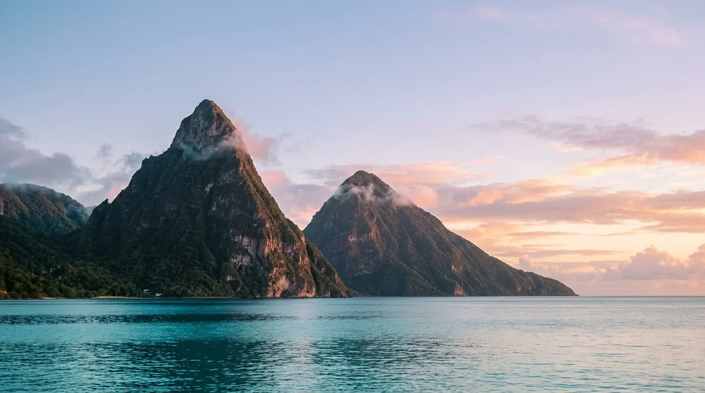 The Pitons of St Lucia rising from the sea at first light, two volcanic peaks emerging from turquoise water with a fringe of dark green forest at the base.
