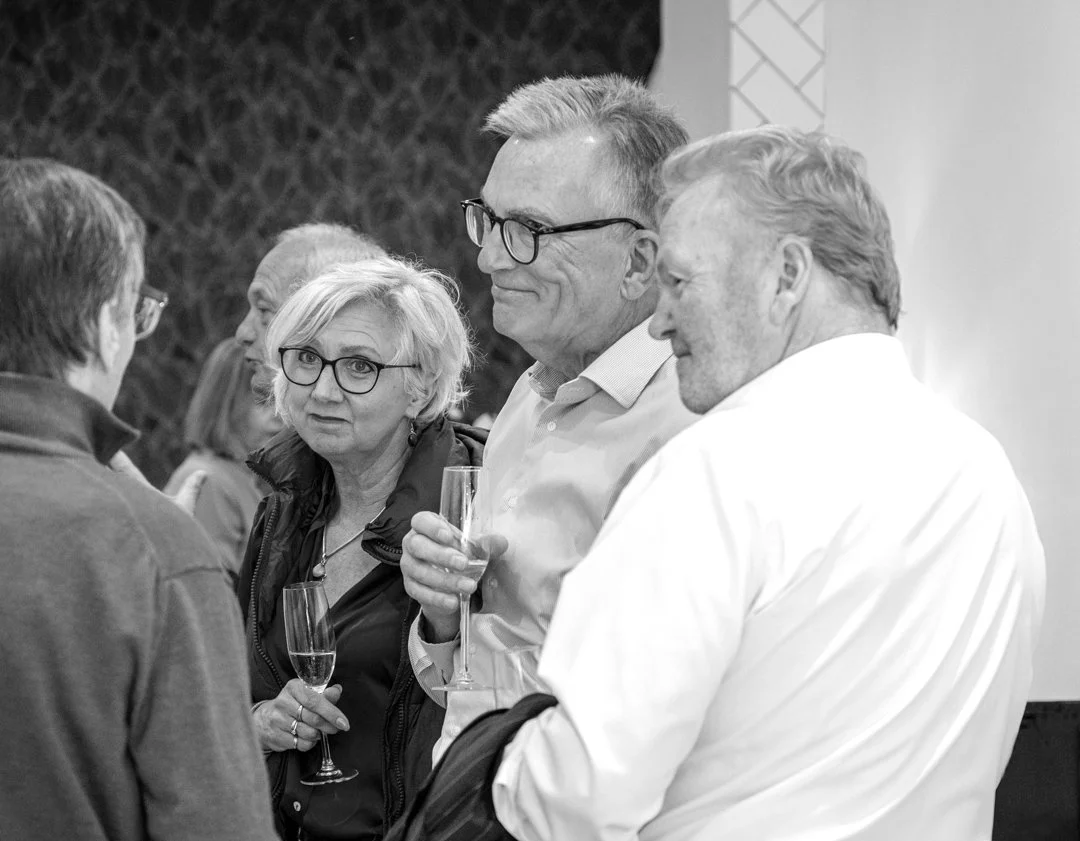 Group of people at a social gathering, holding glasses of champagne, engaging in conversation, indoors.