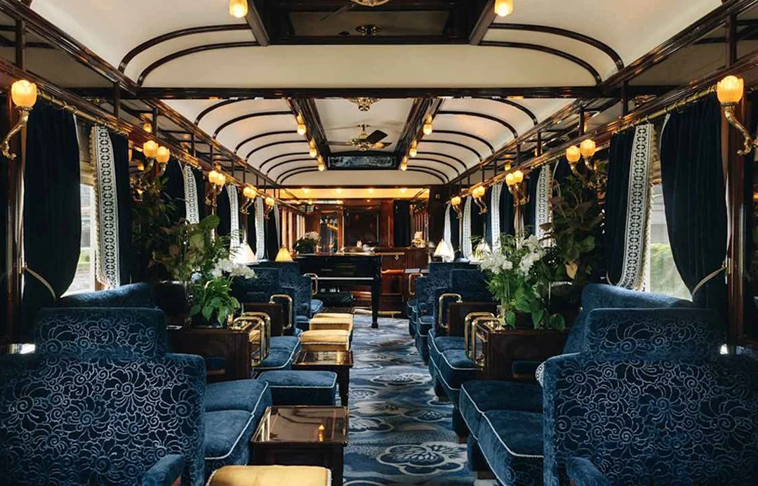 A luxury interior train carriage featuring blue velvet seats and a grand piano.