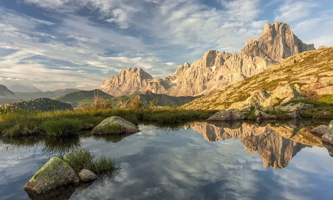 A mountain view looking across the Dolomites in Italy with clear water pool in the foreground.