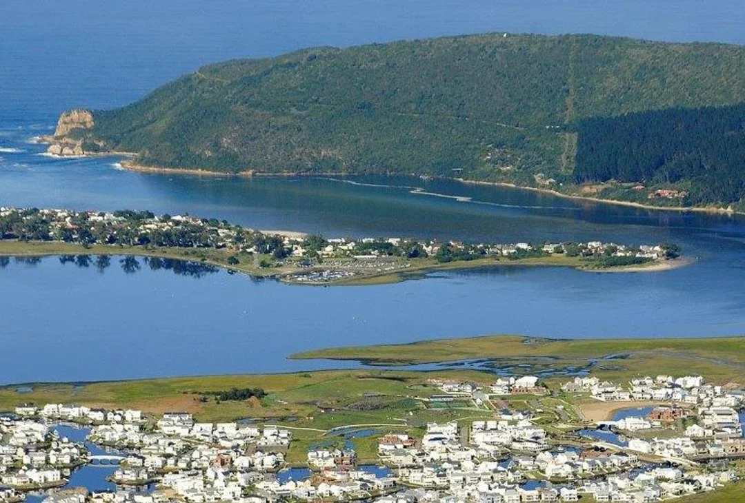A calm lagoon meeting the sea at a wide river mouth, low hills on either side and pale afternoon light on the water.