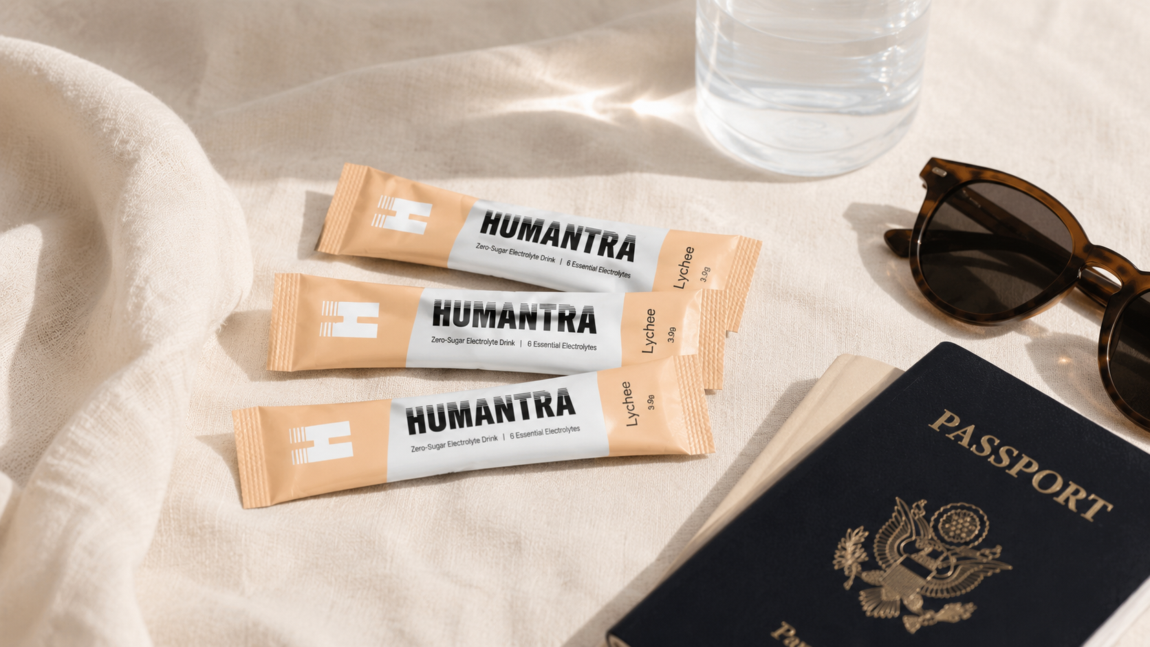 A strip of electrolyte sachets and a glass of water on a pale linen surface beside a passport and sunglasses, soft daylight.