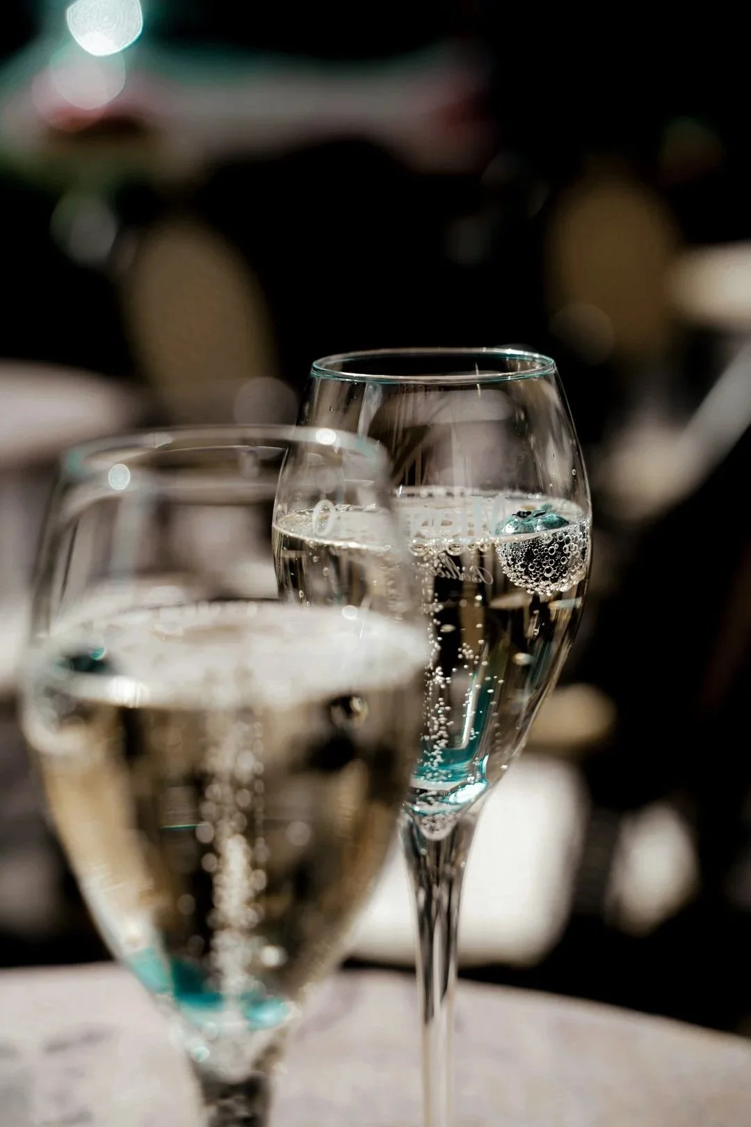 Close-up of two filled champagne glasses with bubbles, with a blurred background.
