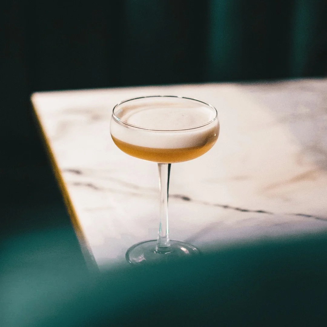 A cocktail in a coupe glass on a table with a blurred background.