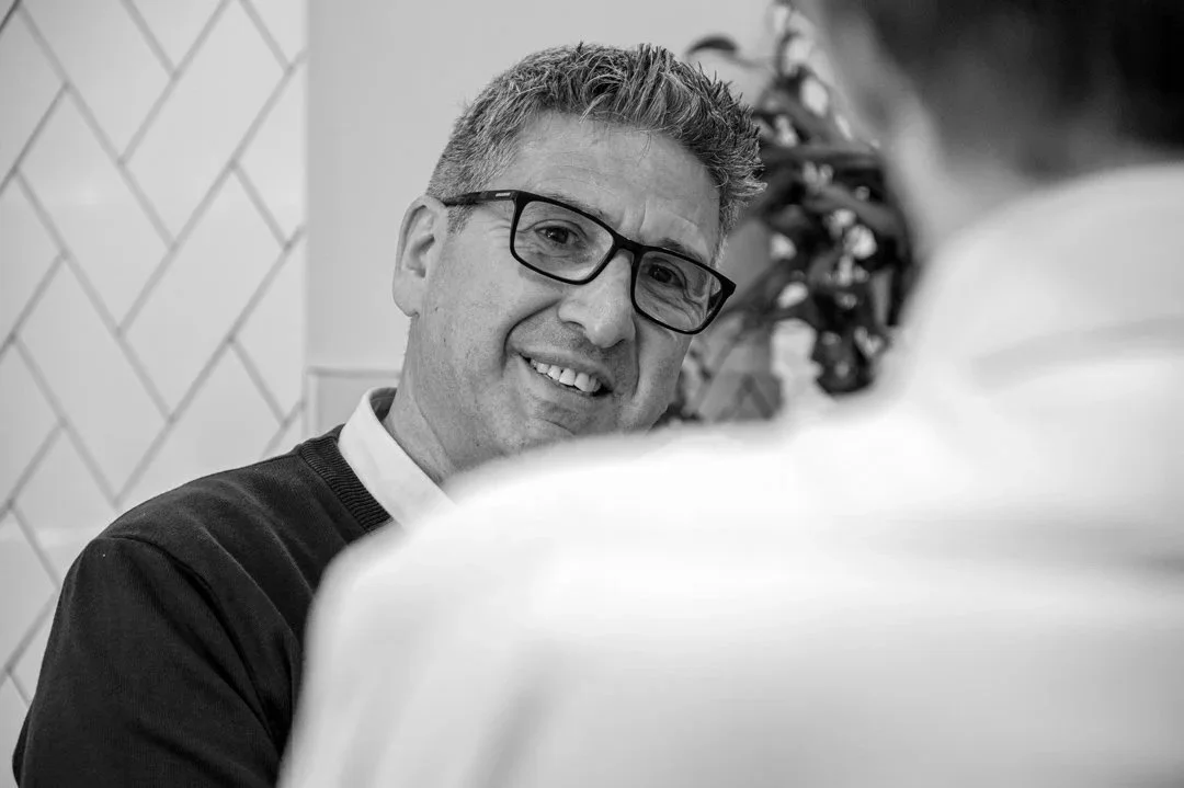 Man with glasses smiling and talking to a woman in a white top, indoors, in black and white.