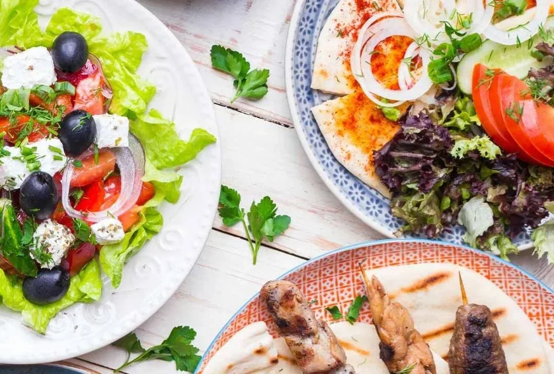 A spread of Greek canapés on a pale table, grilled skewers, halloumi and small meze plates, warm light.