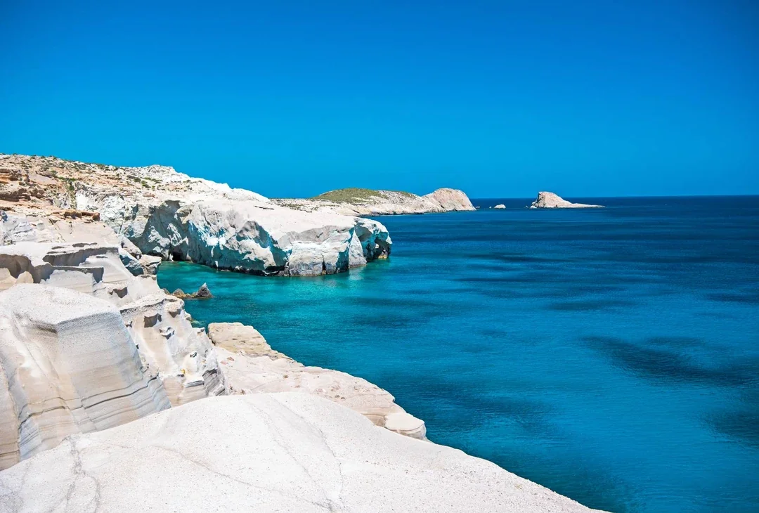 Smooth white volcanic rock at Sarakiniko on Milos, curving down into clear turquoise water under a blue sky.