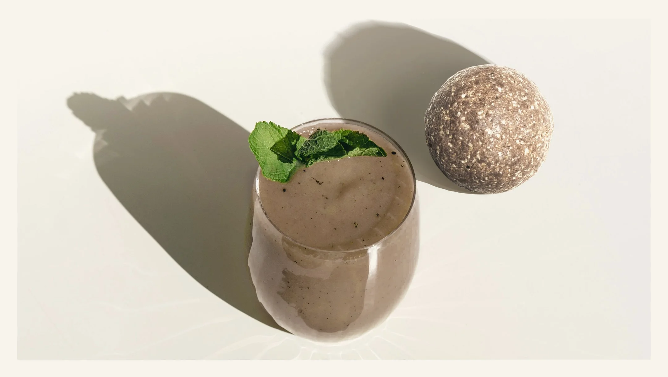 A glass of Chocolate Orange Smoothie made with nourishing ingredients including organic cacao, guarana, oats, pea protein, orange oil, nut butters and dates.