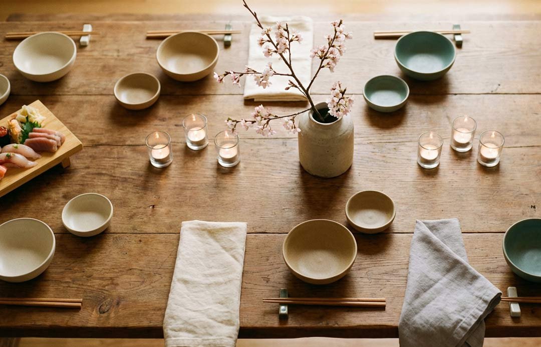 A tabel is set with Japanese food, bowls, chopsticks, napkins and flowers.
