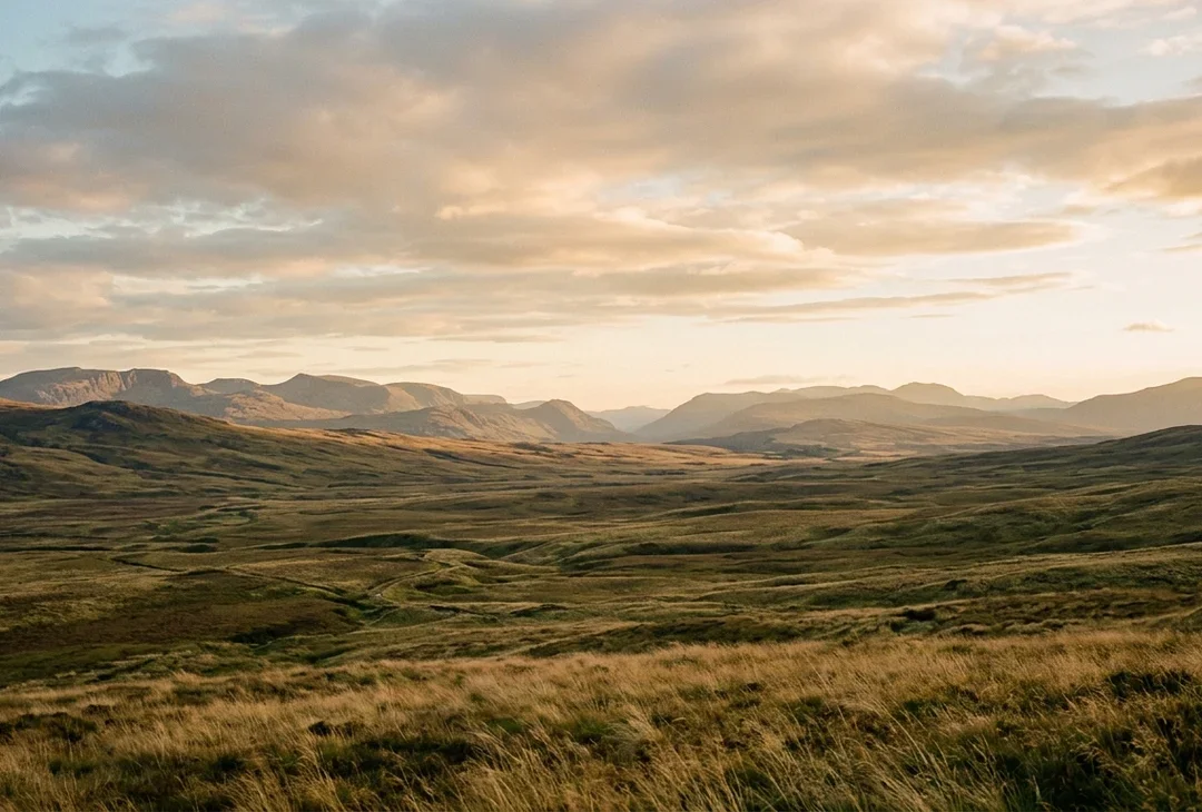 An atmospheric far-reaching landscape at golden hour, open plains beneath distant hills, no people, no landmark.