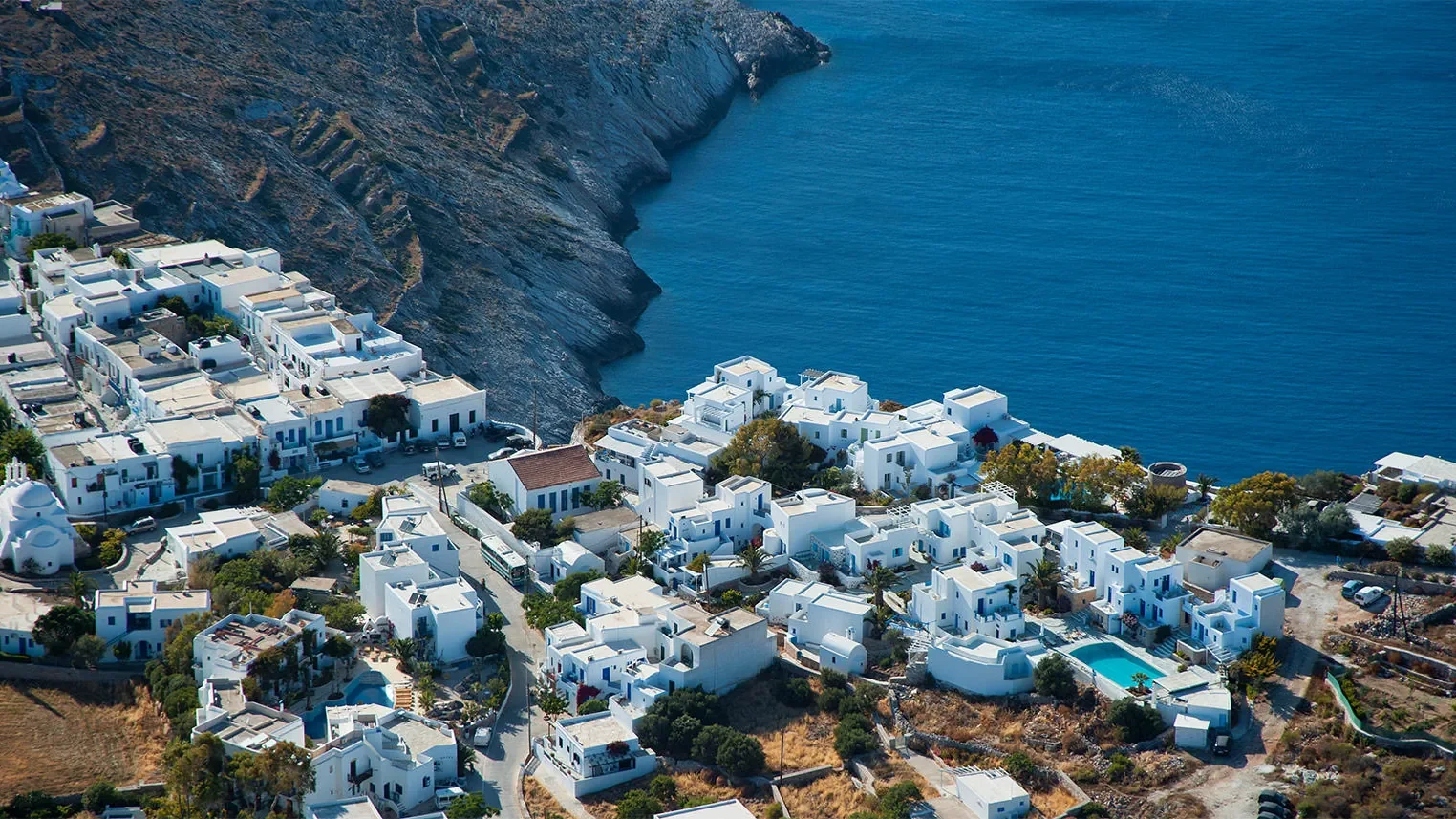 Whitewashed houses of Folegandros' Chora on the cliff edge, above a dark headland and deep blue sea.