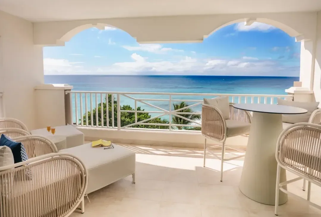 A quiet resort terrace on Barbados with empty chairs facing the sea in soft winter light, no people.