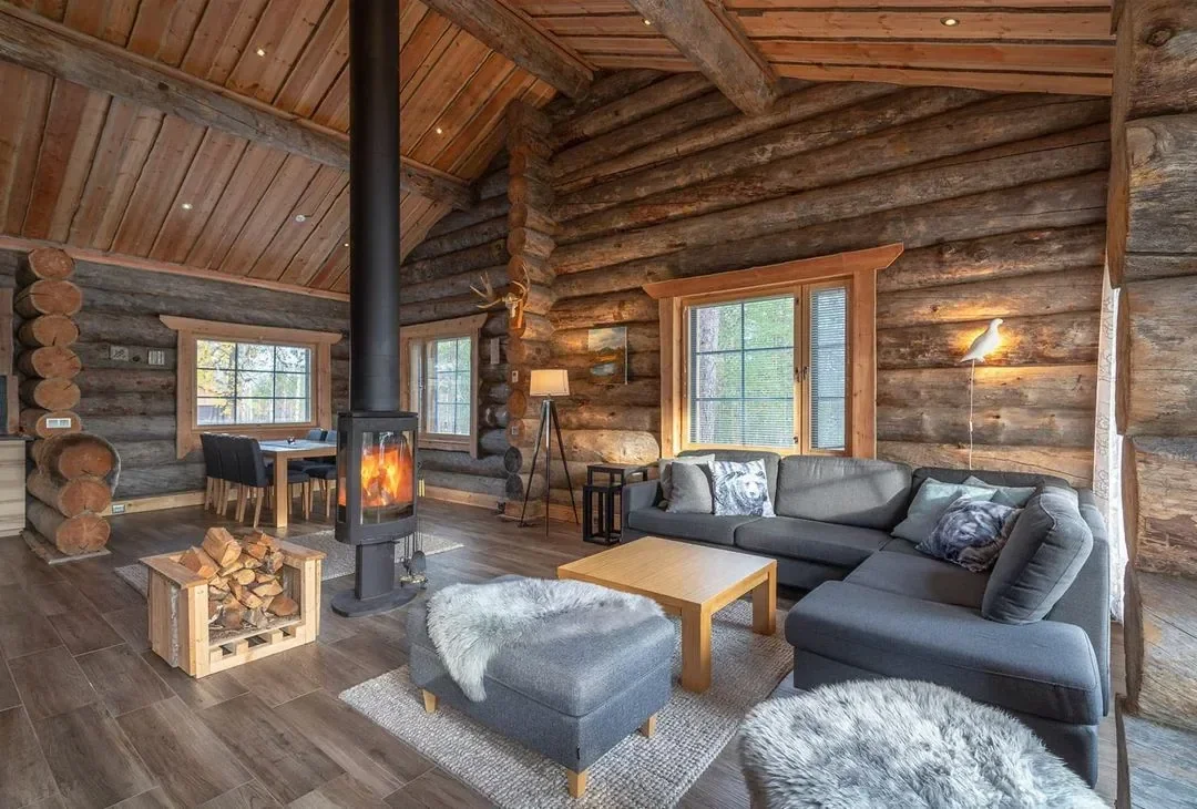 A warmly lit wooden cabin interior in Lapland with a window looking out onto snow, no people, evening light.