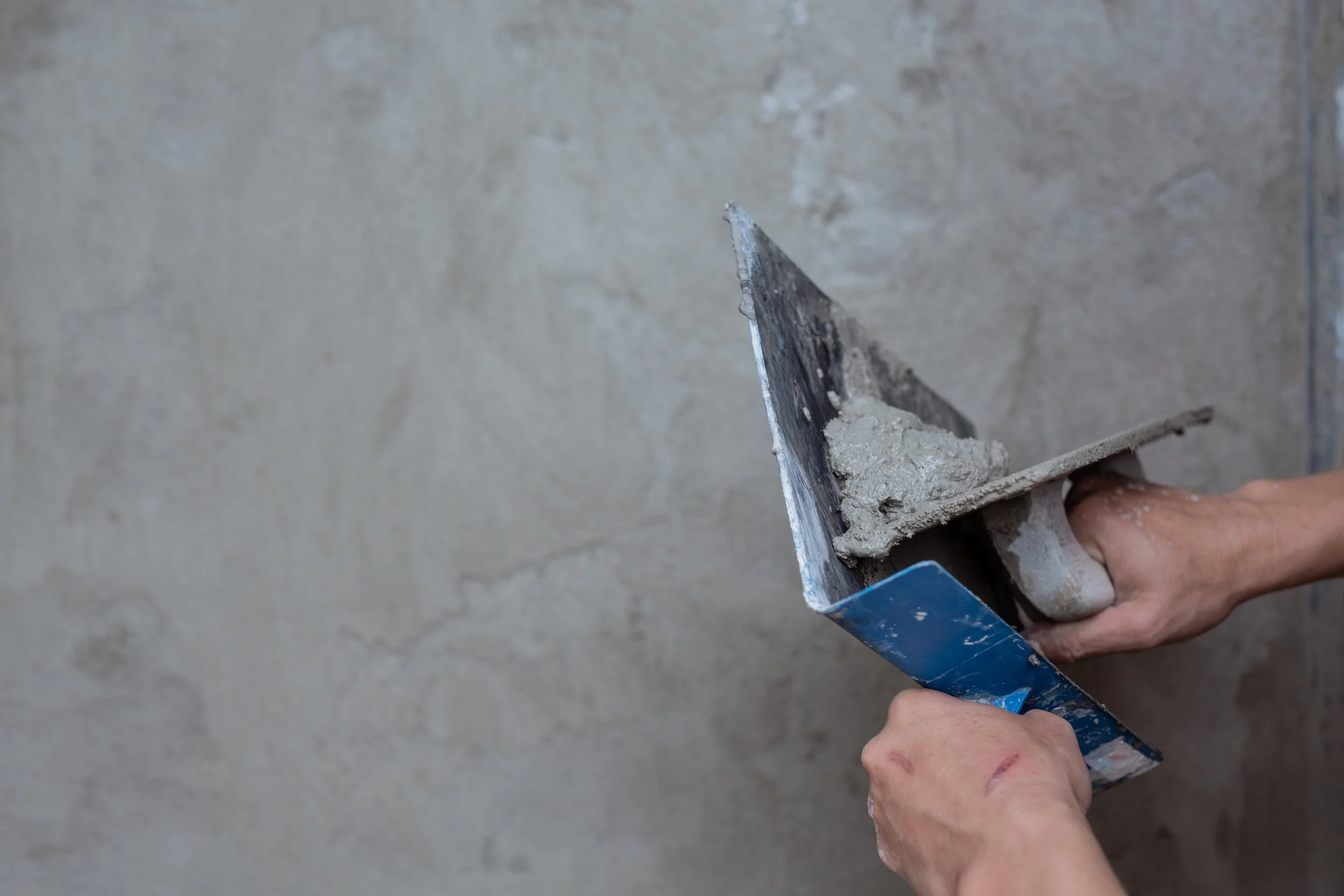 A person using a trowel to spread wet cement on a wall during construction or renovation work.