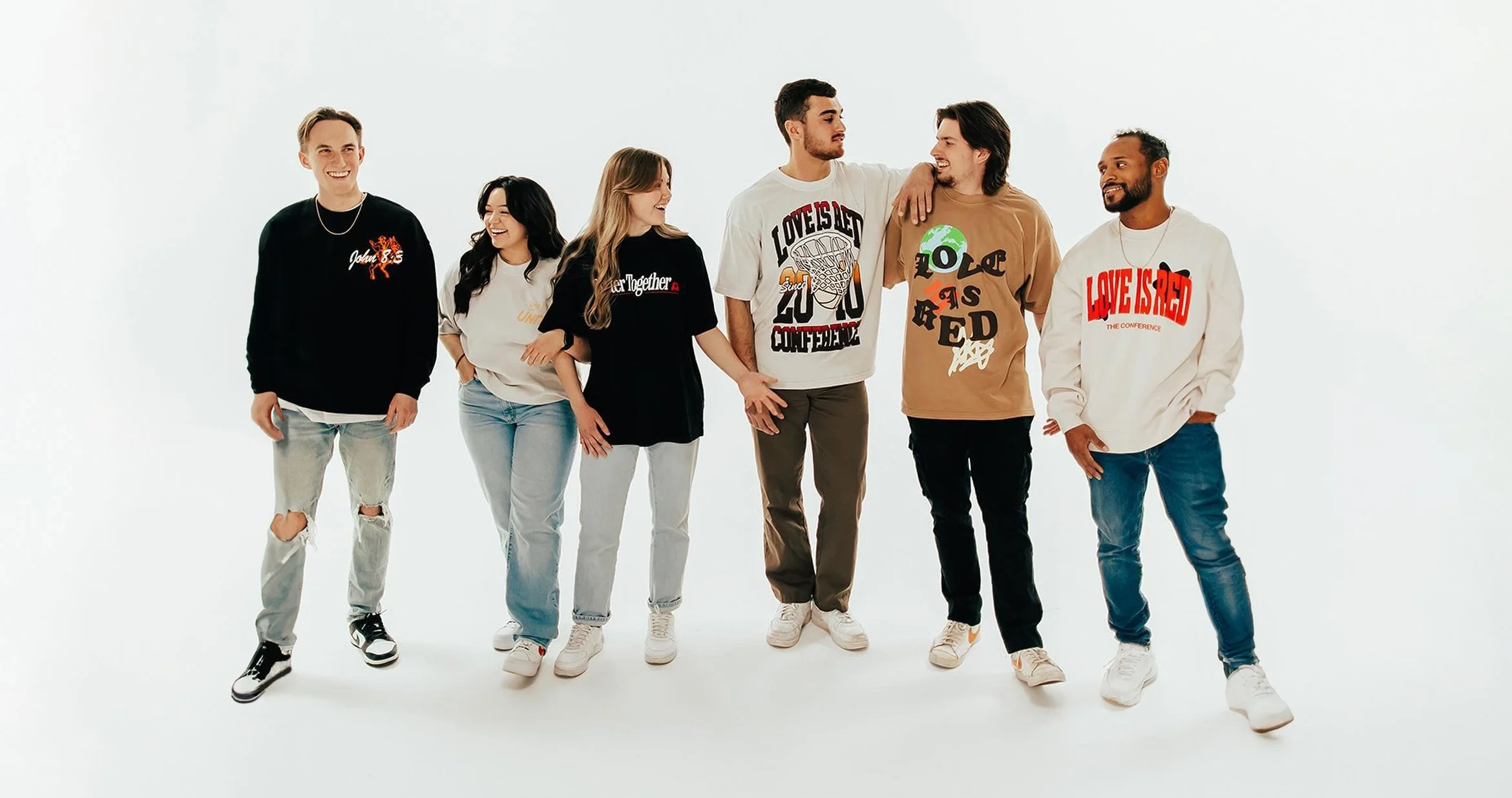 Group of seven diverse friends standing together, smiling and talking, against a plain white background, all wearing custom church merch apparel created by ChurchMerch by utees.