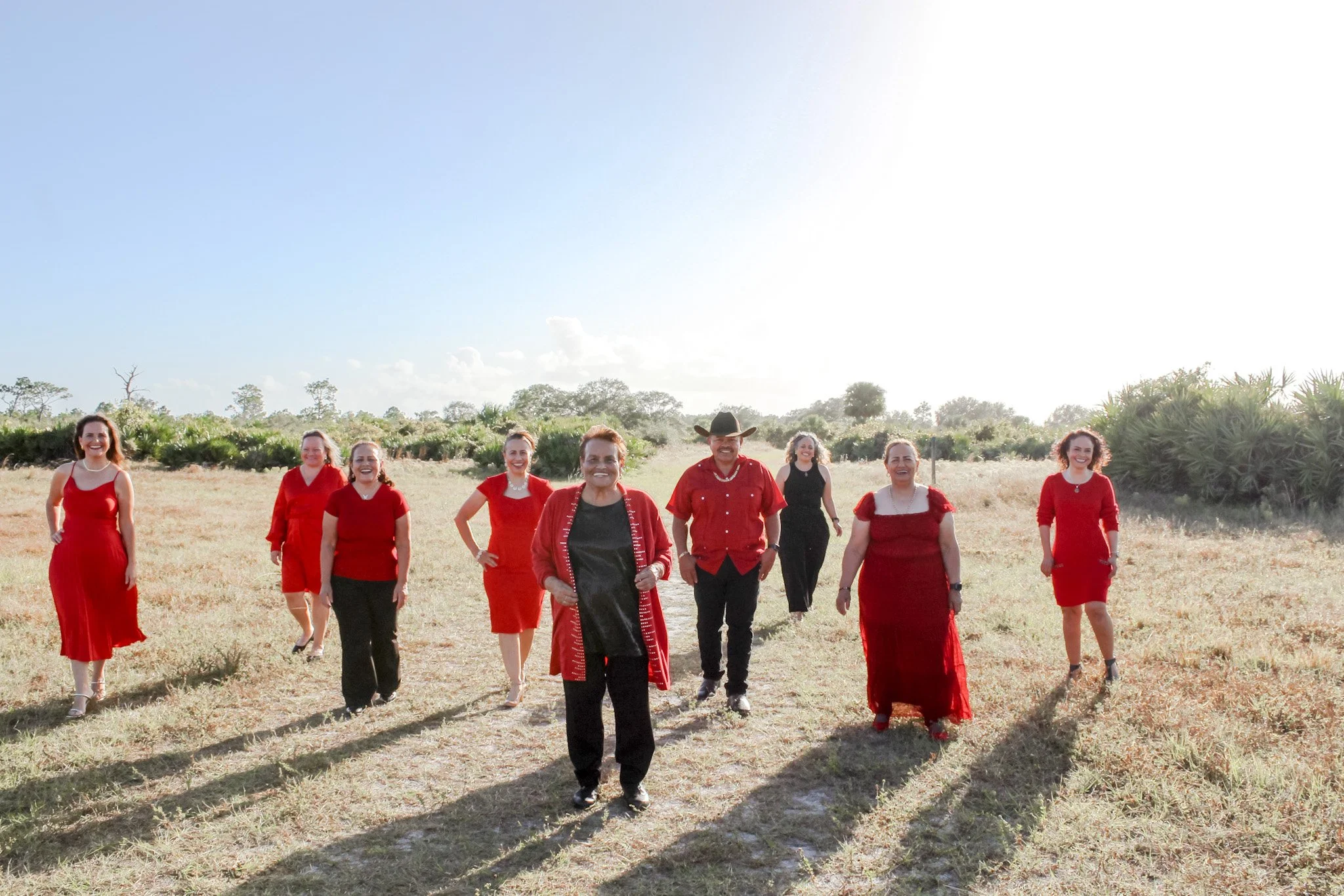 Group of ten people dressed in red and black walking in an open grassy field under a clear sky, smiling and enjoying the sunny day.