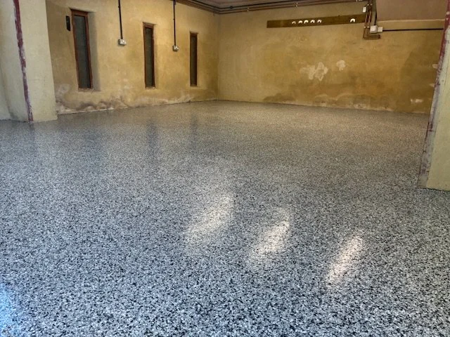 Empty room with a speckled epoxy floor, yellow walls, and small windows along the side. Pipes and electrical wiring are visible.Resin floors The Wye Valley, Herefordshire, South Wales, West Midlands, west, cardiff, birmingham, bristol
