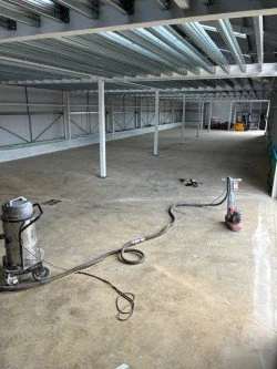 Empty industrial or commercial space with a concrete floor, metal beams, and exposed ceiling, being cleaned with two floor scrubbers.Resin floors The Wye Valley, Herefordshire, South Wales, West Midlands, west, cardiff, birmingham, bristol 