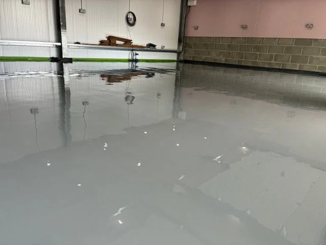 Freshly poured gray epoxy floor in a garage or industrial space, with some tools and a clock on the wall.Resin floors The Wye Valley, Herefordshire, South Wales, West Midlands, west, cardiff, birmingham, bristol