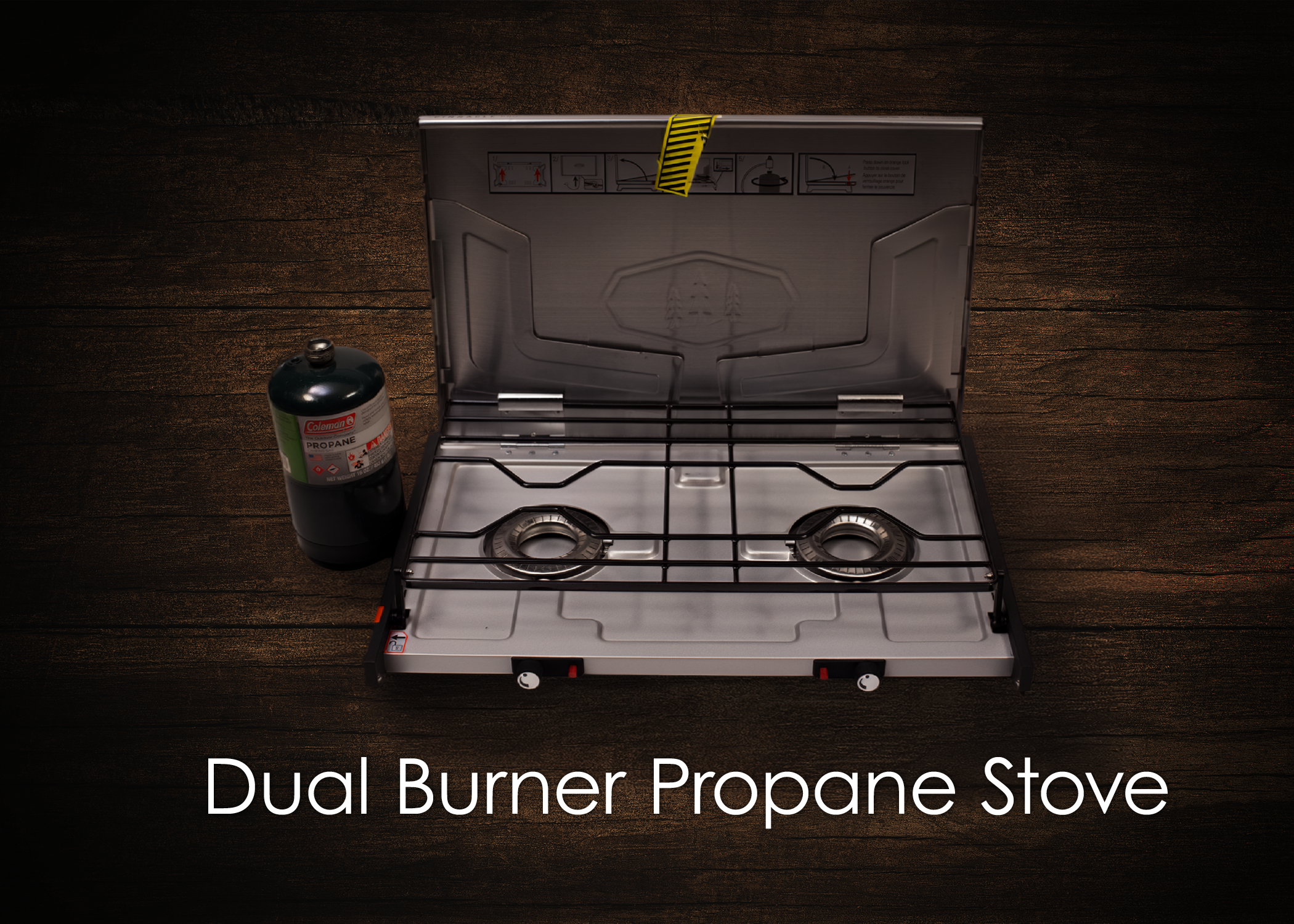 A dual burner propane stove with a tank of propane gas next to it, set on a wooden surface.
