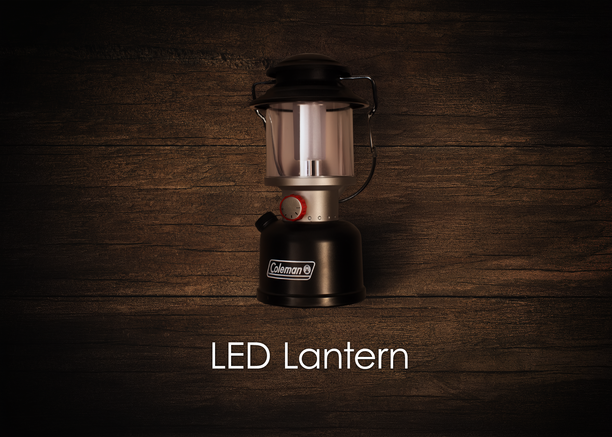 A black Coleman LED lantern with a metal handle and a red knob, placed on a dark wooden surface, with the text "LED Lantern" below it.
