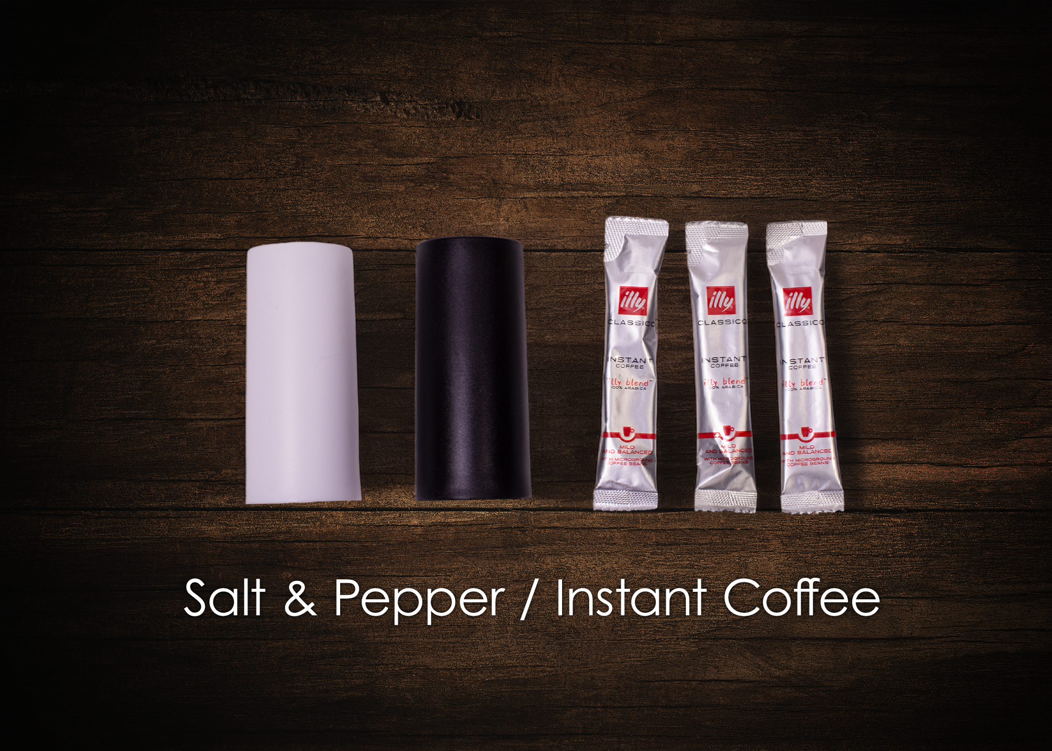 Salt and pepper shakers next to three packets of instant coffee on a wooden surface with the caption 'Salt & Pepper / Instant Coffee' at the bottom.