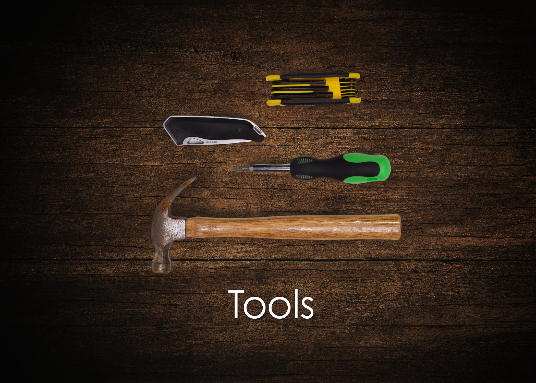 A carpenter's hammer, a utility knife, a screwdriver with a green handle, a multi-bit screwdriver set, and a wood surface with the word 'Tools' written on it.