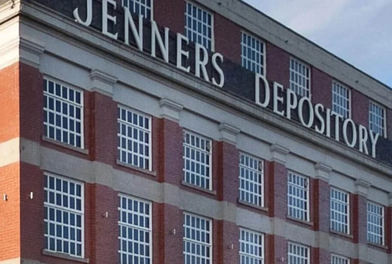 Close-up view of a brick building with white-framed windows and a large sign on the top that reads "JENNERS DEPOSITORY."