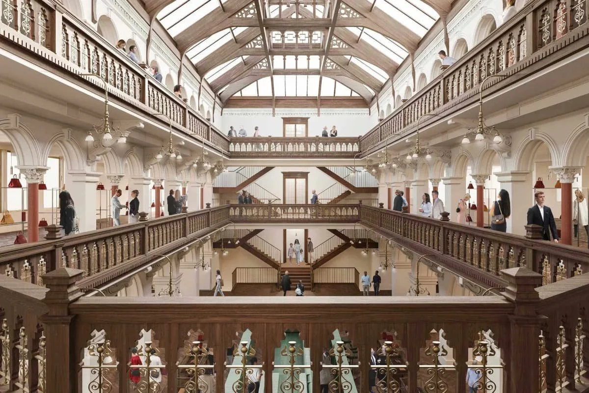 Interior view of a multi-story building with wooden railings, staircases, and large windows, filled with people walking and standing on the balconies and staircases.