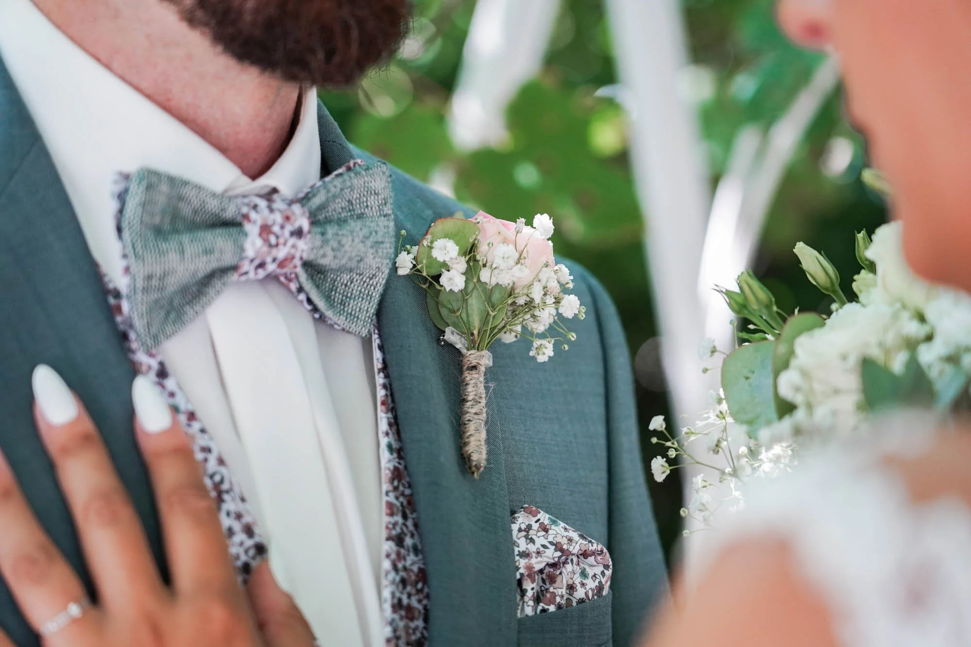 Costume marié bleu-vert avec boutonnière fleurs et nœud papillon motif floral.