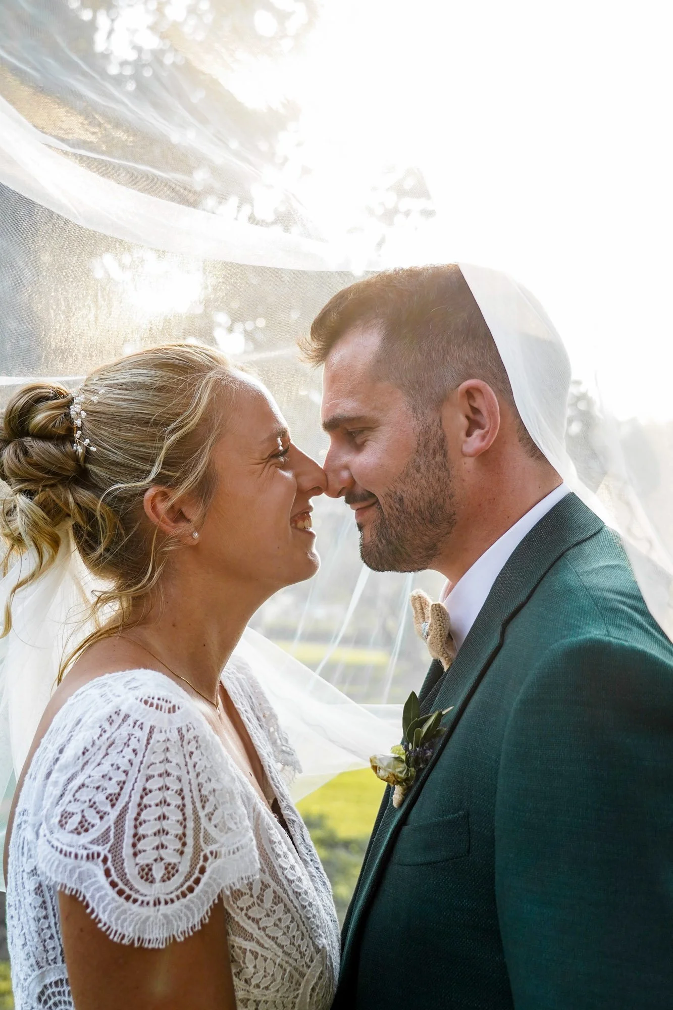 Un couple marié, un homme et une femme, se regardent avec tendresse sous un voile de mariée, à l'extérieur.