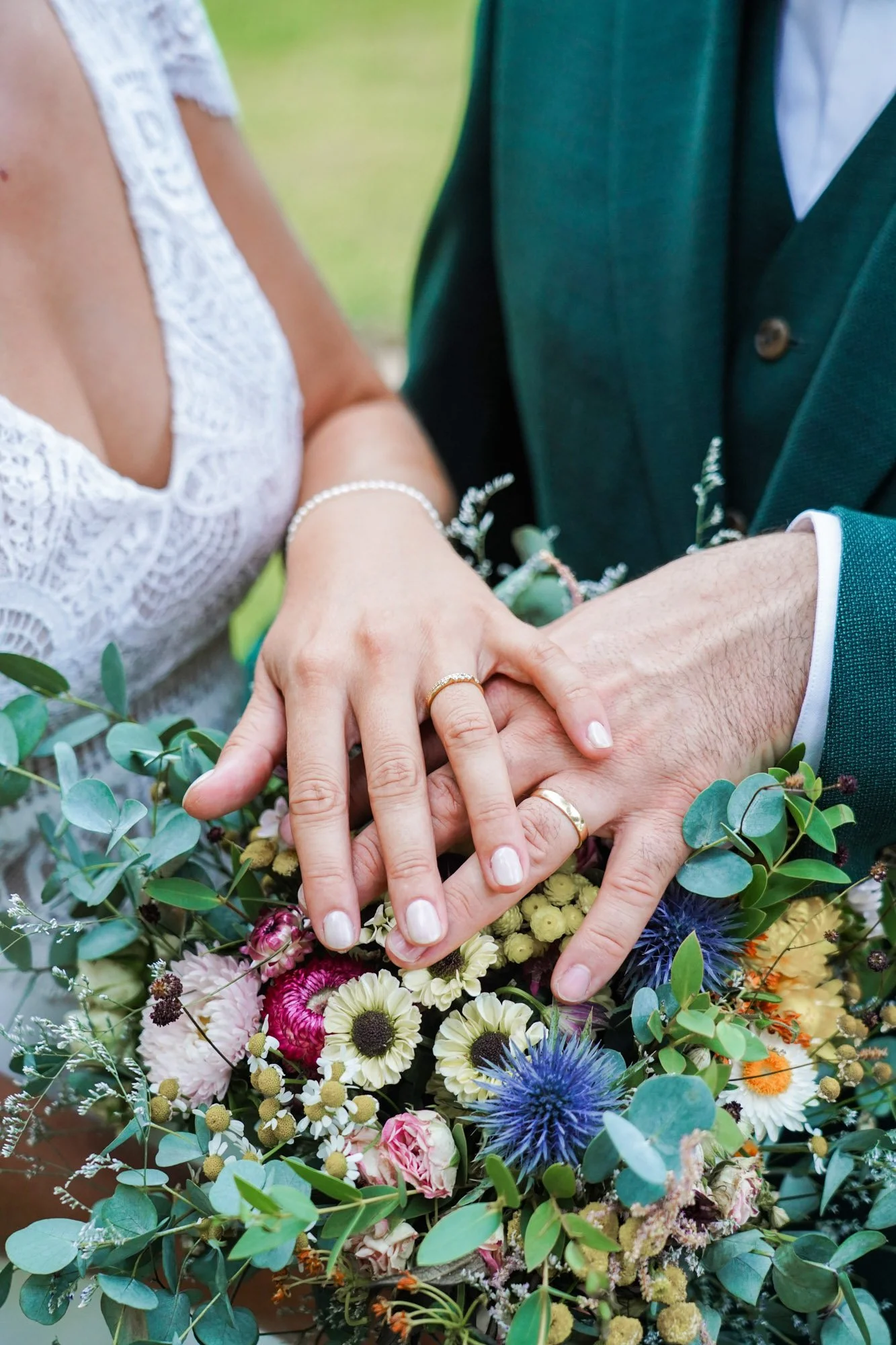 Mains couple marié avec alliances sur bouquet de fleurs colorées.